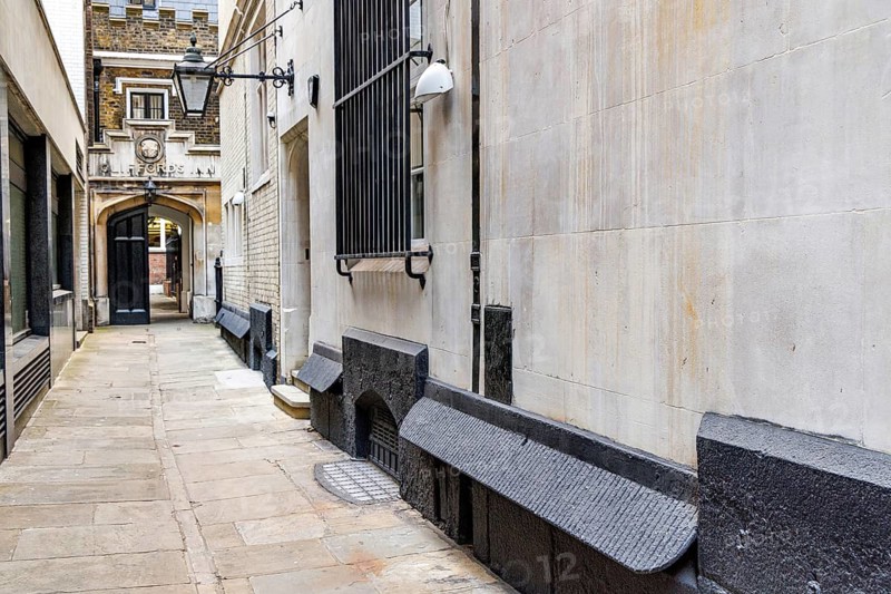 Secret London. A quiet stone paved passage at Clifford's Inn leads towards the historic gatehouse and a wall mounted lamp, its base lined with sloped black ledges fitted in the Victorian era to prevent public urination against the walls of the former Inn of Chancery. London, England, United Kingdom