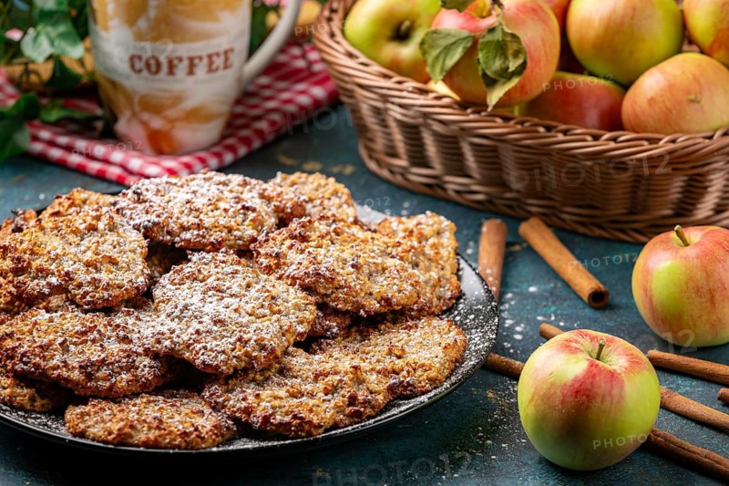Apple cookies sprinkled with powdered sugar, coffee cup and apples behind