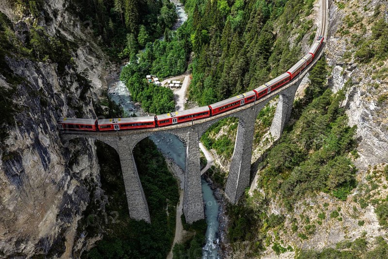 Red train of the Rhaetian railroad line, Bernina Express, passing the Landwasser Viaduct, arch bridge over Landwasser river, aerial view, Switzerland