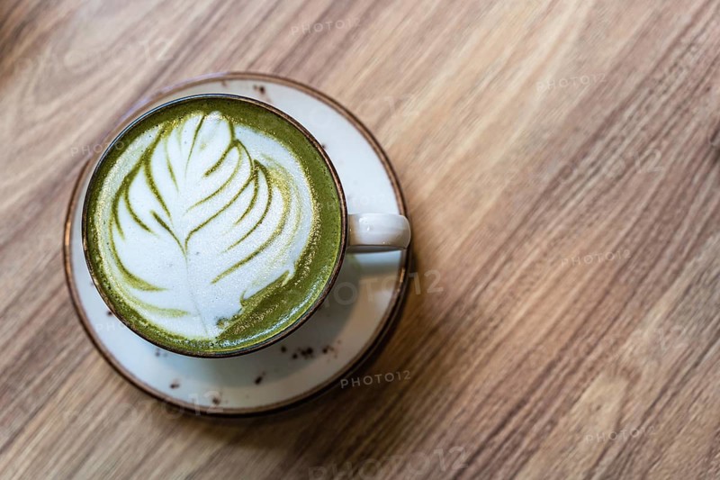A cup of matcha latte on the table. Latte art on a green background, A matcha latte with leaf design latte art in a ceramic cup on a wooden table