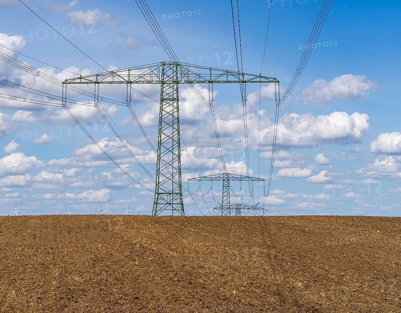 Wide agricultural landscape with freshly plowed fields and high-voltage lines as well as wind turbines on the horizon, Uckermark, Brandenburg, Germany