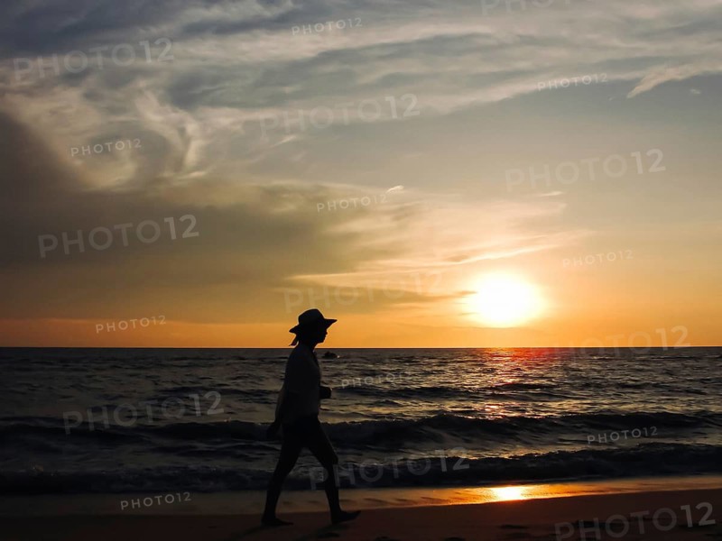 A woman walking along the beach during sunset, silhouetted against the orange sky and ocean