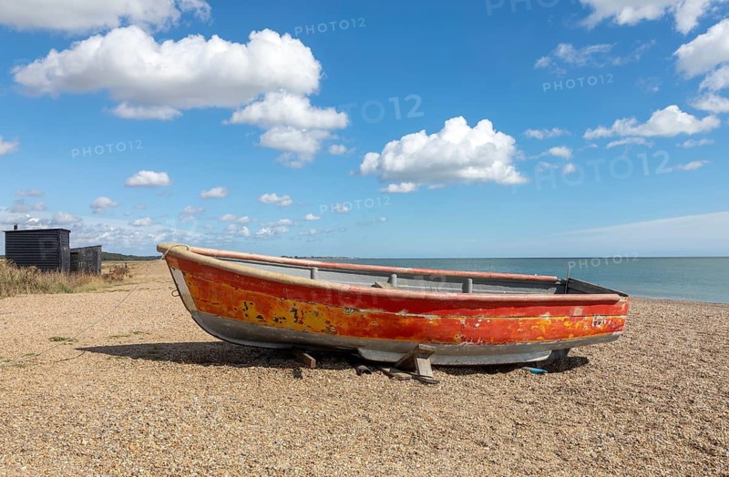 Coastal landscape of old red boat on beach with blue sky cumulus cloud, Dunwich, Suffolk, England, UK