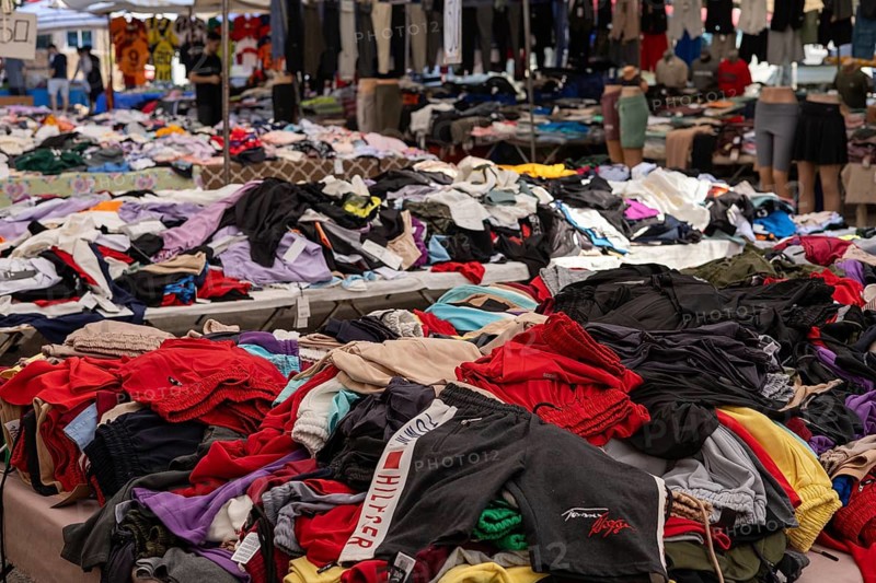 Assorted clothing piled on tables at an outdoor market