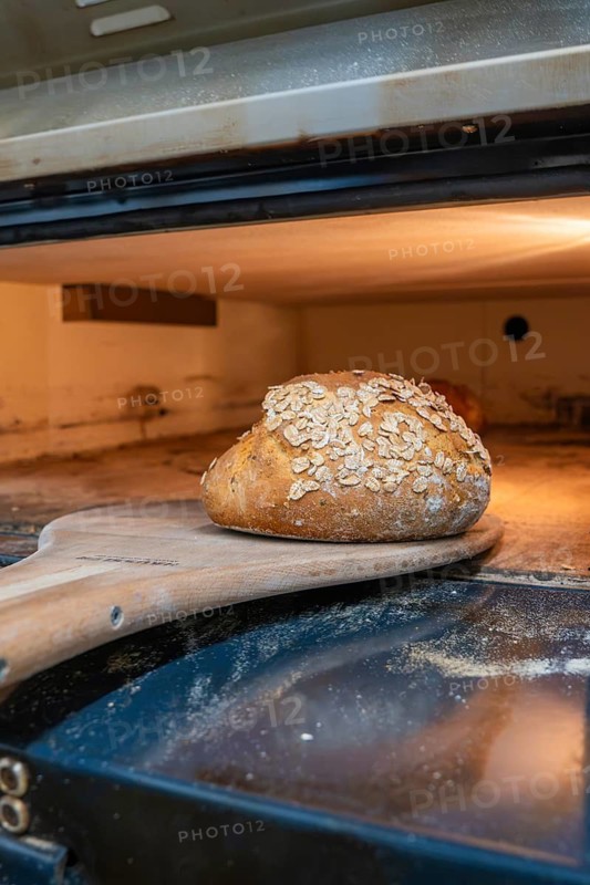 A golden brown bread with oats is taken out of the oven with a wooden shovel, bake bread, Haselstaller Hof, Gechingen, Calw district, Germany