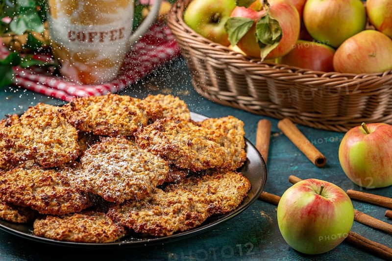 Apple cookies are sprinkled with powdered sugar, coffee cup and apples behind