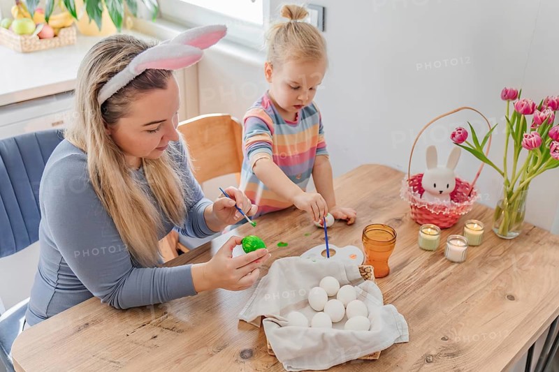 Mother and toddler girl daughter painting Easter eggs at home in modern kitchen. family tradition, spring celebration and holiday preparation
