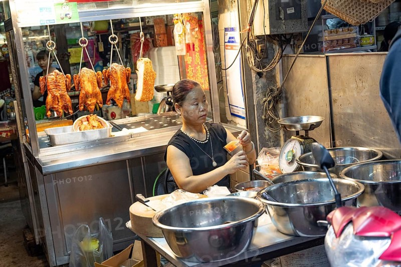 Bangkok, Thailand. August 24th 2026. A local woman prepares a sauce at a street food stall with Chinese roasted ducks hanging in the window, Chinatown, Bangkok, Thailand, Asia