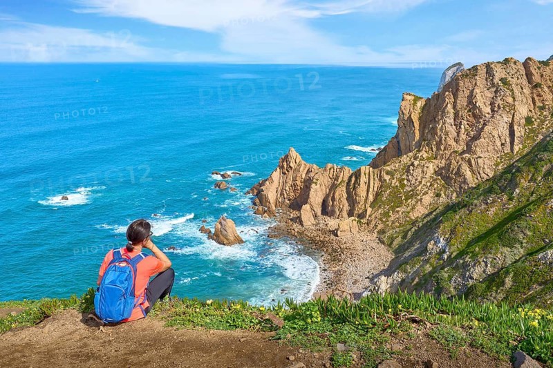 Woman hiking on the coastline of Cabo Raso Lighthouse, Atlantic West coast, Portugal