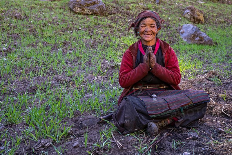 Portrait, elderly friendly smiling Nepalese woman, local of the Tsumba Tibetan ethnic group folding her hands in greeting Namaste, Tsum Valley, Himalayas, Nepal