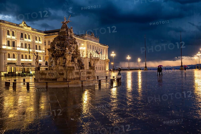 Illuminated square Piazza Unità d'Italia with Fontana dei Quattro Continenti fountain, Palazzo del Lloyd Triestino, with reflection, dramatic clouds, blue hour, old town, Trieste, Friuli-Venezia Giulia region, Italy