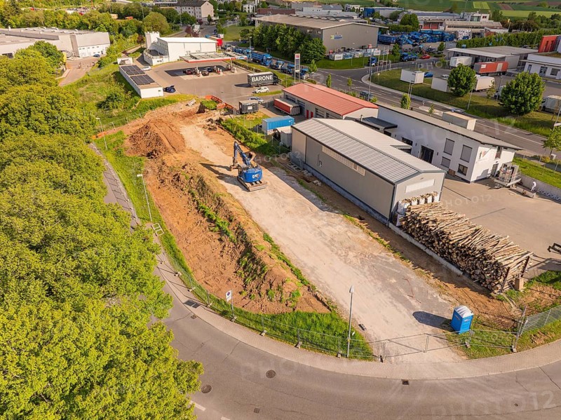 Construction site with excavator and pile of wood next to a road and commercial buildings, Parkhaus Bau, Calw, Germany