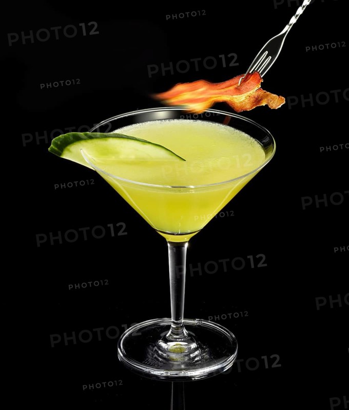 Yellow-green cocktail with black background, cucumber slice and ham as garnish, studio shot