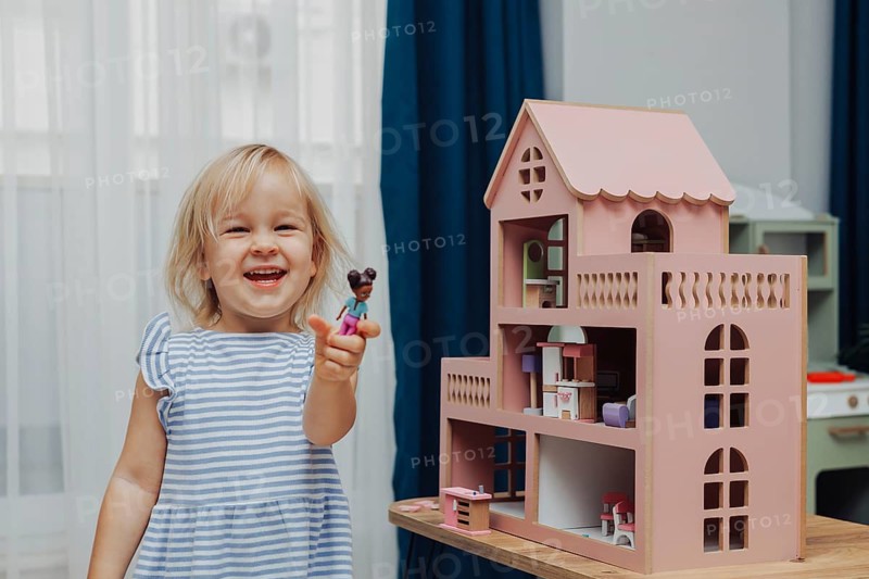 Child girl in blue dress arranges wooden furniture in a doll house. Concept of education during the game