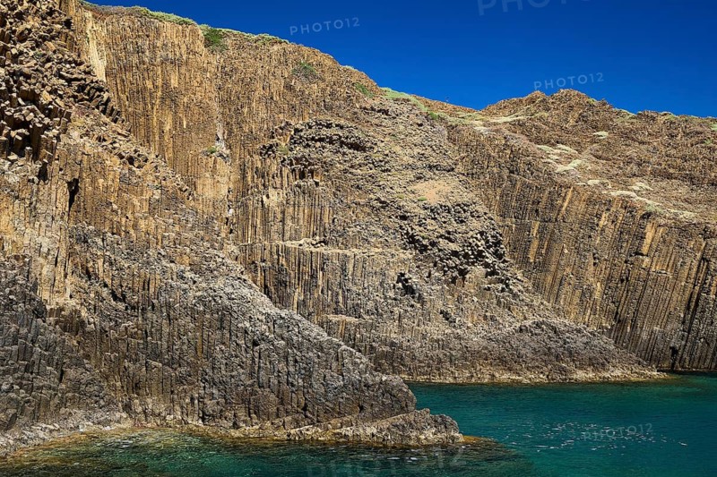 Towering basalt columns on a rocky coast with clear blue sky and calm sea, Glaronisia, Glaronesia, Milos, islets, hexagonal basalt columns, north of Milos, destination by boat, Cyclades, Greek Islands, Greece