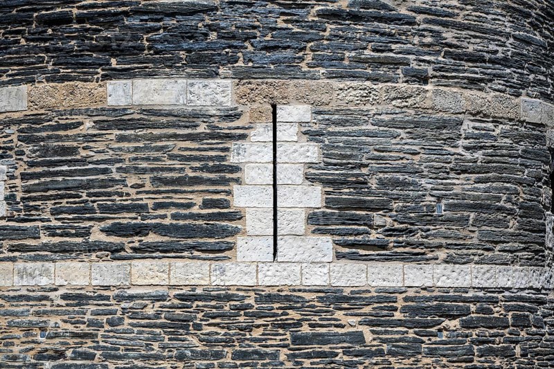Detailed view of one of the mighty defensive towers with narrow, vertical loopholes, built of slate and limestone from Château d'Angers, Angers Castle, Angers, Maine-et-Loire department, Pays de la Loire region, France