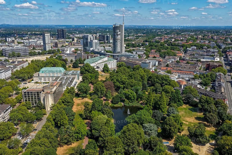 Essen, North Rhine-Westphalia, Germany - City panorama of Essen, skyline with front city garden with lake and fountain, on the left the Sheraton Essen Hotel and the Philharmonic, in the back the Aalto Theatre and the Evonik Tower skyscrapers, former RWE Tower, the Post Bank and at the very back the town hall. Stadtgarten Essen is Essen's oldest publicly accessible green space. It is located south of Essen Central Station in the Südviertel district, between the Aalto Theatre, the Philharmonic and the neighboring Rüttenscheid district. Parks and gardens in the Ruhr area