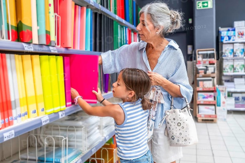 Grandmother and granddaughter perusing a bright stationery aisle, searching for school organization items and choosing colorful folders during their back to school shopping trip
