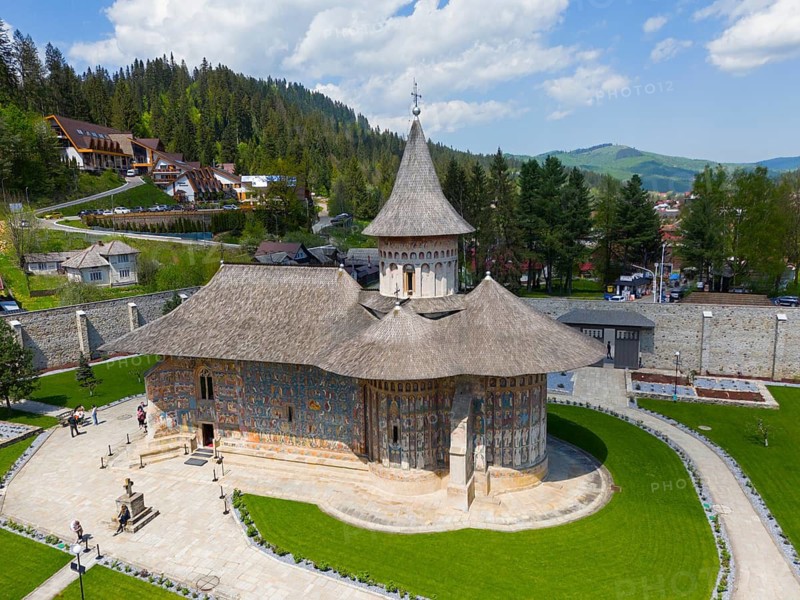 Orthodox church with frescoes surrounded by green countryside and wooded hills under clear blue sky, aerial view, Saint George Monastery, Voronet Monastery, Voronet Monastery, UNESCO World Heritage Site, Suceava County, Bukovina Region, Romania
