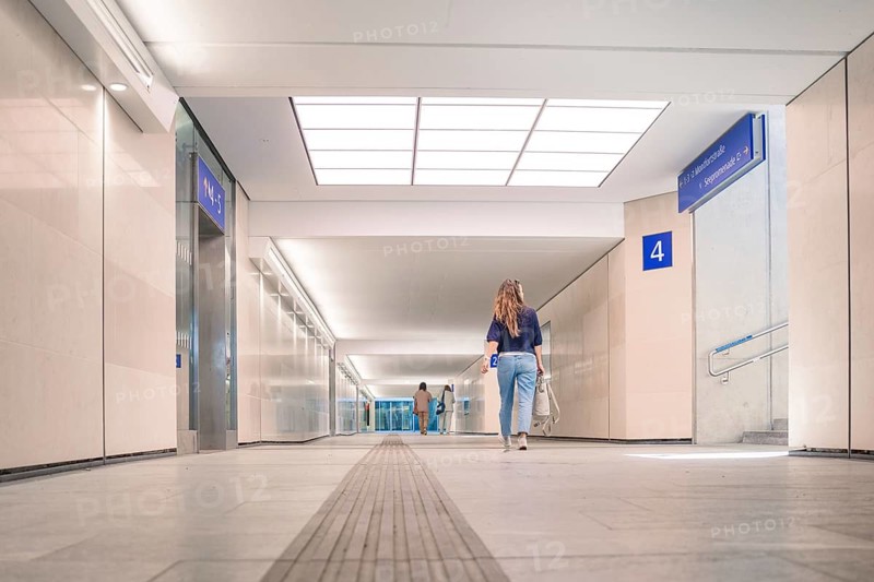 Modern hall with people walking under bright lighting, showing structural and tidy design features, Agri PV Bau, Germany