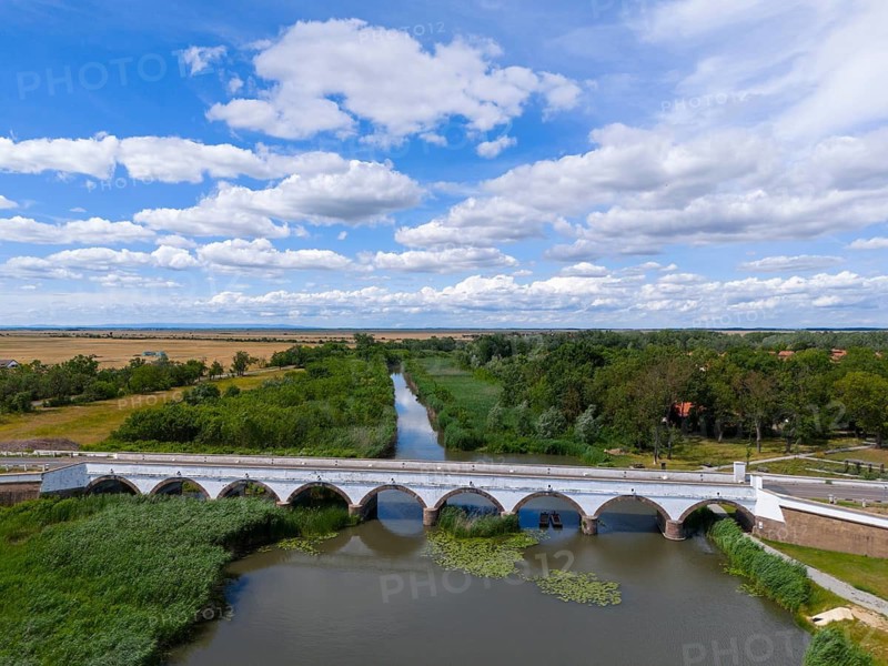 View over a bridge over a river with green surroundings and a sky full of clouds, aerial view, nine-arched stone bridge, Kilenclyukú híd, Hortobagy, Hortobagy National Park, Hortobágyi Nemzeti Park, Hortobágyi Csillagoségbolt Park, Puszta, steppe area, UNESCO Biosphere Reserve, Hungary