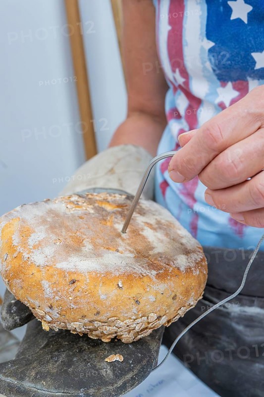 Woman measures the temperature of a loaf of bread with a measuring device device in her hand, baking bread, Haselstaller Hof, Gechingen, Calw district, Germany