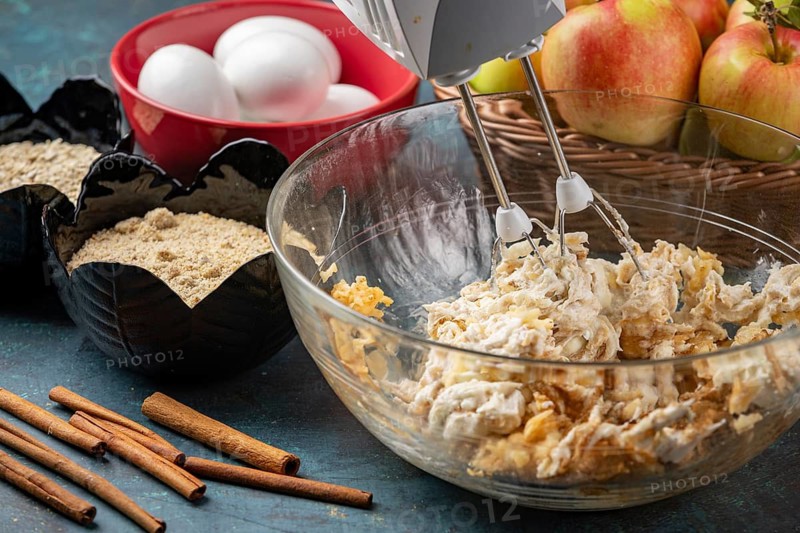 Grated apples and quark are mixed in a bowl, surrounded by other baking ingredients