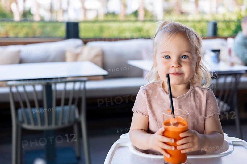 Girl toddler drinking fresh orange carrot juice in outdoor cafe