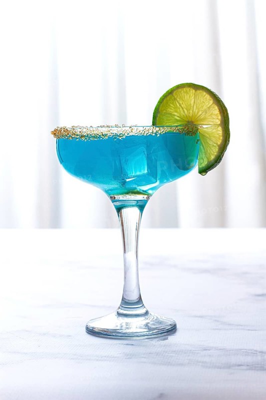 Bright blue cocktail with a slice of lime on a marble surface