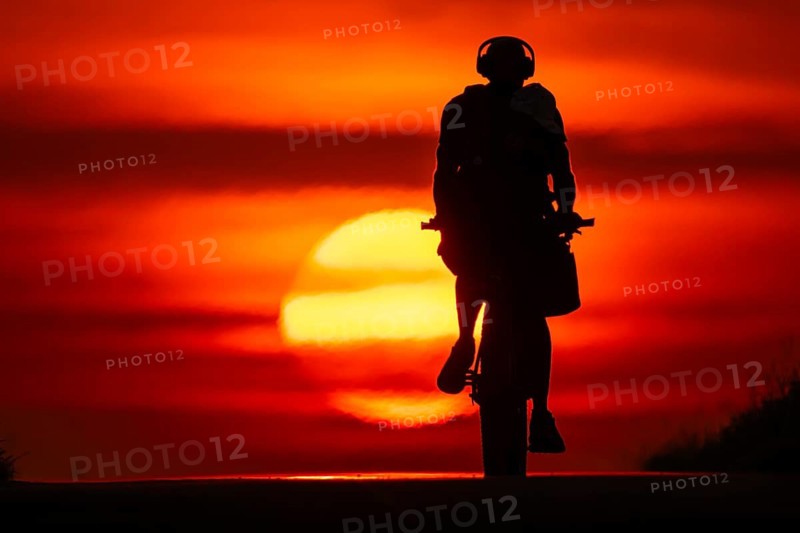 A cyclist rides towards the rising sun on a dirt road near Frankfurt am Main, Frankfurt am Main, Hesse, Germany