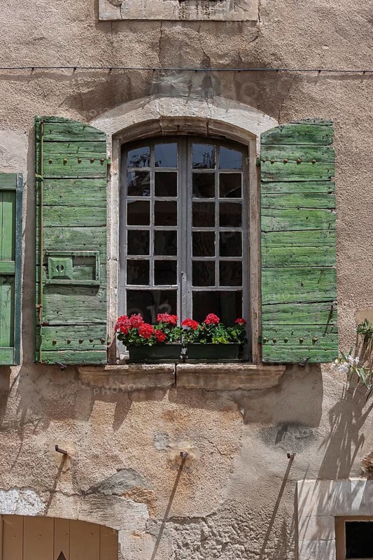 Window with green shutters and red geraniums on an old stone wall, Provence, France