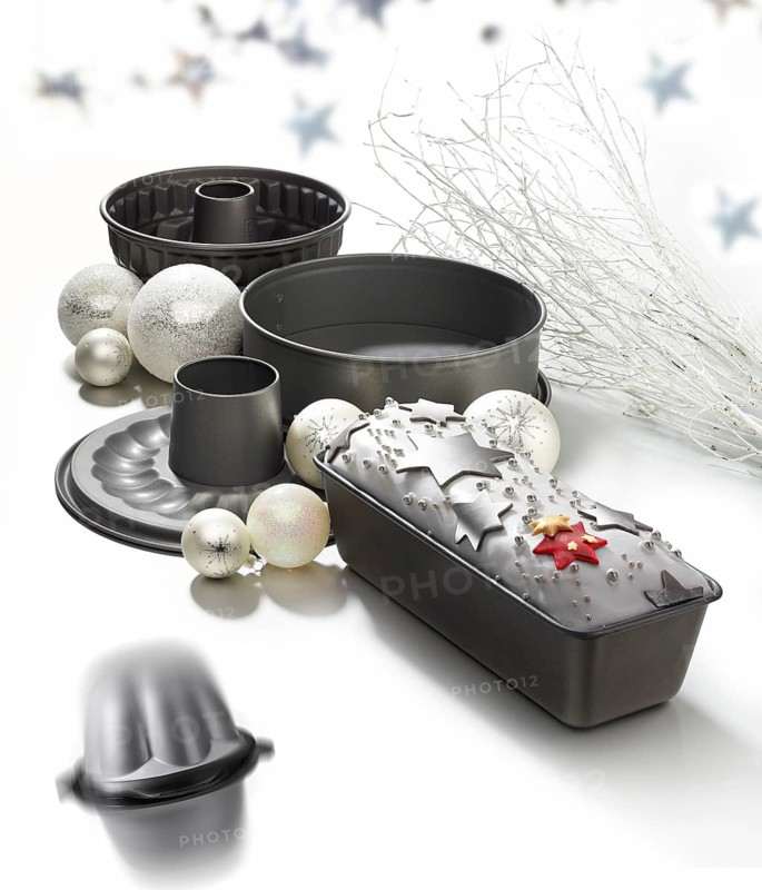 Various baking pans, asterisks and Christmas balls as decoration, against a white background, studio shot