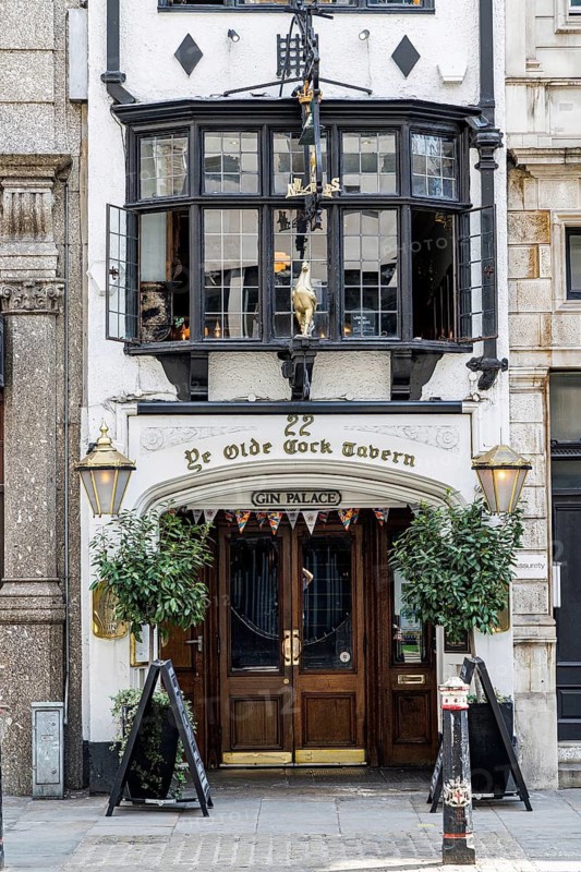 The timber and gilt entrance of Ye Olde Cock Tavern welcomes visitors at 22 Fleet Street, a Grade II listed public house with origins before the seventeenth century that was rebuilt on its present site in the 1880s after its original premises were needed for a Bank of England branch. London, England, United Kingdom
