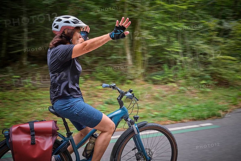 Active senior woman having fun practicing handsfree cycling on a bike path through a peaceful forest, showing balance, confidence, freedom and active aging