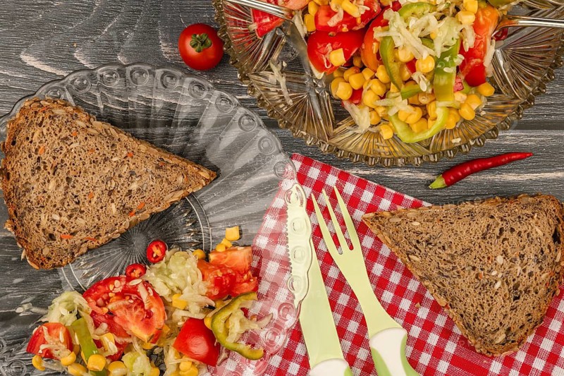 Salad plate with slice of brown bread and fresh vegetables on a rustic wooden table with checkered cloth