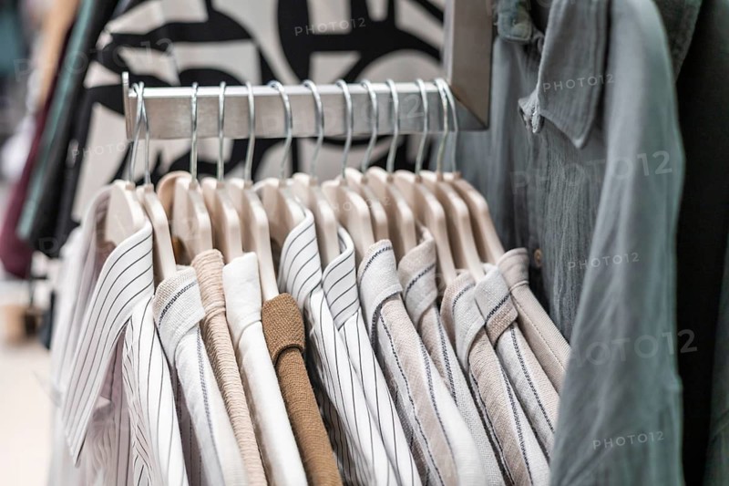 A rack displaying neatly arranged striped and solid shirts in a retail store. The shirts are hanging on wooden hangers, showcasing various colors and patterns