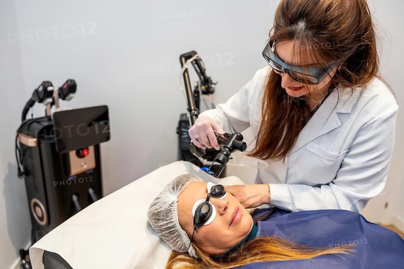 Woman undergoing a professional laser skin treatment on her face, with a skilled medical aesthetician operating the device while both wear protective eyewear in a modern clinic