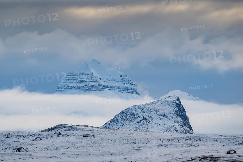 Large rock behind clouds cover one of the three mountains Tee Kroner, Kongsfjord or Kongsfjorden, Spitsbergen archipelago, Svalbard, Norway