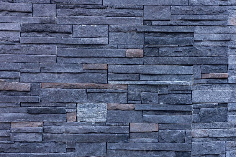 A textured wall made of dark stone bricks arranged in a pattern. The stones vary in size and color, creating a modern and stylish appearance