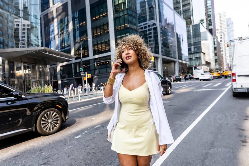 Young woman with curly hair walking confidently on a sunny manhattan city street, communicating on her mobile phone while enjoying the urban lifestyle