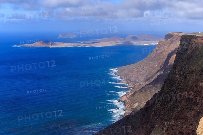 Lanzarote, Canary Islands, Spain, Europe, Mirador de El Risco de Famara, Parque El Bosquecillo, High cliffs drop steeply to the deep blue sea, with islands on the horizon under a blue sky