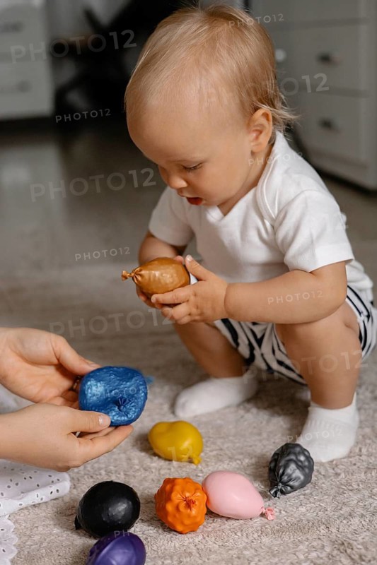 A toddler explores colorful toys with curiosity, emphasizing learning and playful focus in an indoor setting