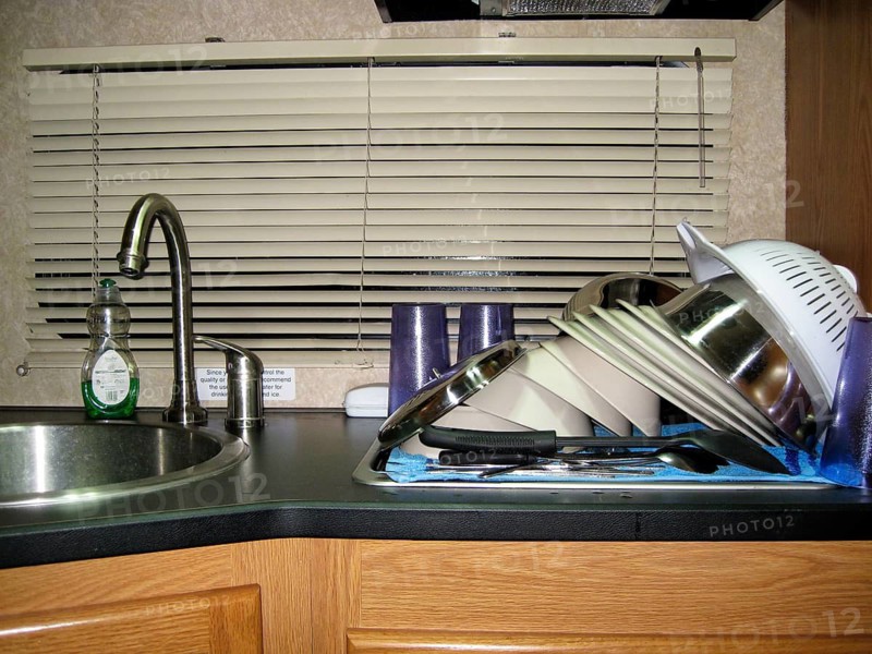 Freshly washed dishes, plates, bowls, cups, silverware, ladle and spatula, pasta colander, stacked to dry on work surface, sink in an RV, camping kitchen, USA
