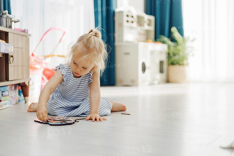 Child girl interacts with a storage unit filled with toys in a sunny indoor space
