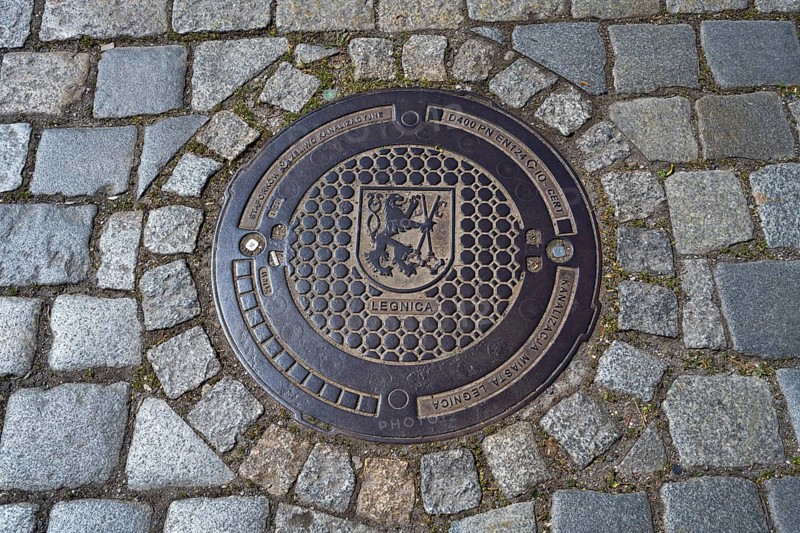 A close-up of a manhole cover on paving stones, decorated with the Legnica coat of arms, manhole cover, Legnica, Legnica, Lower Silesian Voivodeship, Poland