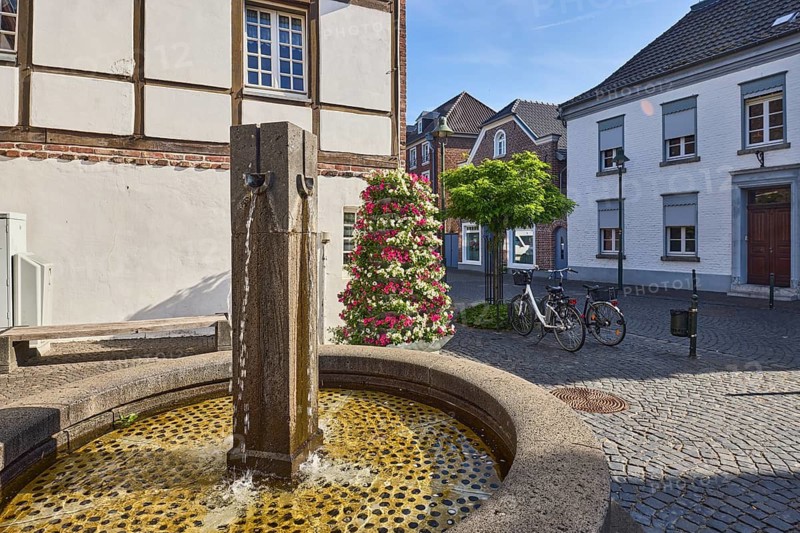 Fountain, old town, historic town center, historic half-timbered house, houses, street, paving stones, flower pots, trees, blue sky, cirrostratus clouds, wine route confluence with Feldstraße, Wachtendonk, Kleve district, North Rhine-Westphalia, Germany