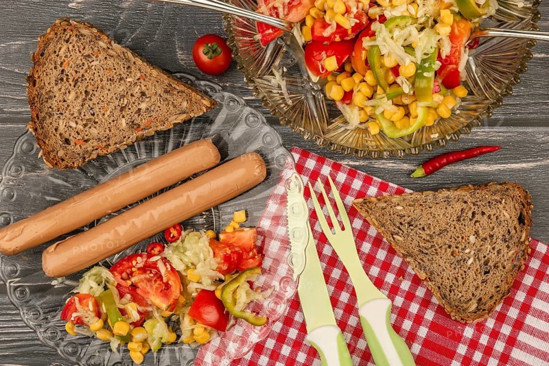 Plate with sausages, salad and brown bread on a table covered with checkered cloth