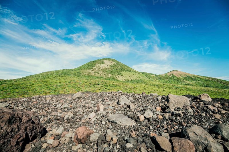 View of a hill surrounded by vegetation against a beautiful blue sky, a beautiful, vegetation-covered hill surrounded by volcanic rocks