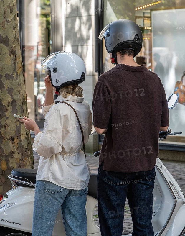 Young couple wearing motorcycle helmets standing next to a Vespa, Frankfurt am Main, Hesse, Germany