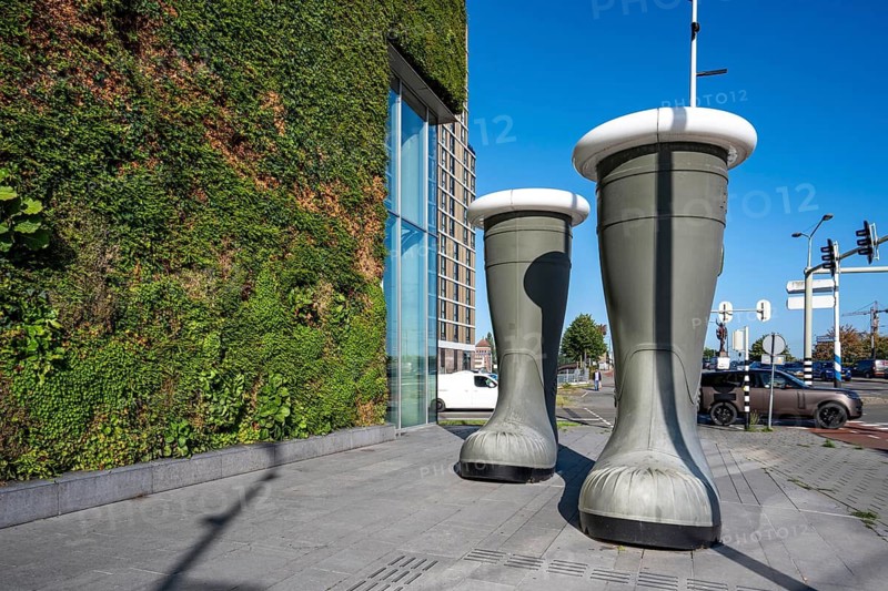 Work of art The Boots of the Hunter, sculpture of 2 large rubber boots that glow in the evening, by Venlo artist Pii Dänen, in front of the green north façade of Stadskontoor Venlo, building of the city administration, from 2016, approx. 2200 square meters of the façade are green, various types of plants hang in plant modules in front of the actual façade, a combined climate concept, a circulatory system, with a greenhouse on the upper floors, thermal energy from The underground parking garage, a so-called solar chimney, cools the building air in summer and heated in winter, rainwater is used to irrigate the green building façade, the entire project was built according to the cradle-to-cradle concept, Venlo, Limburg, the Netherlands